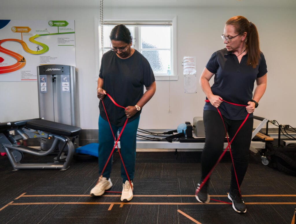 Two women exercising with red resistance bands indoors